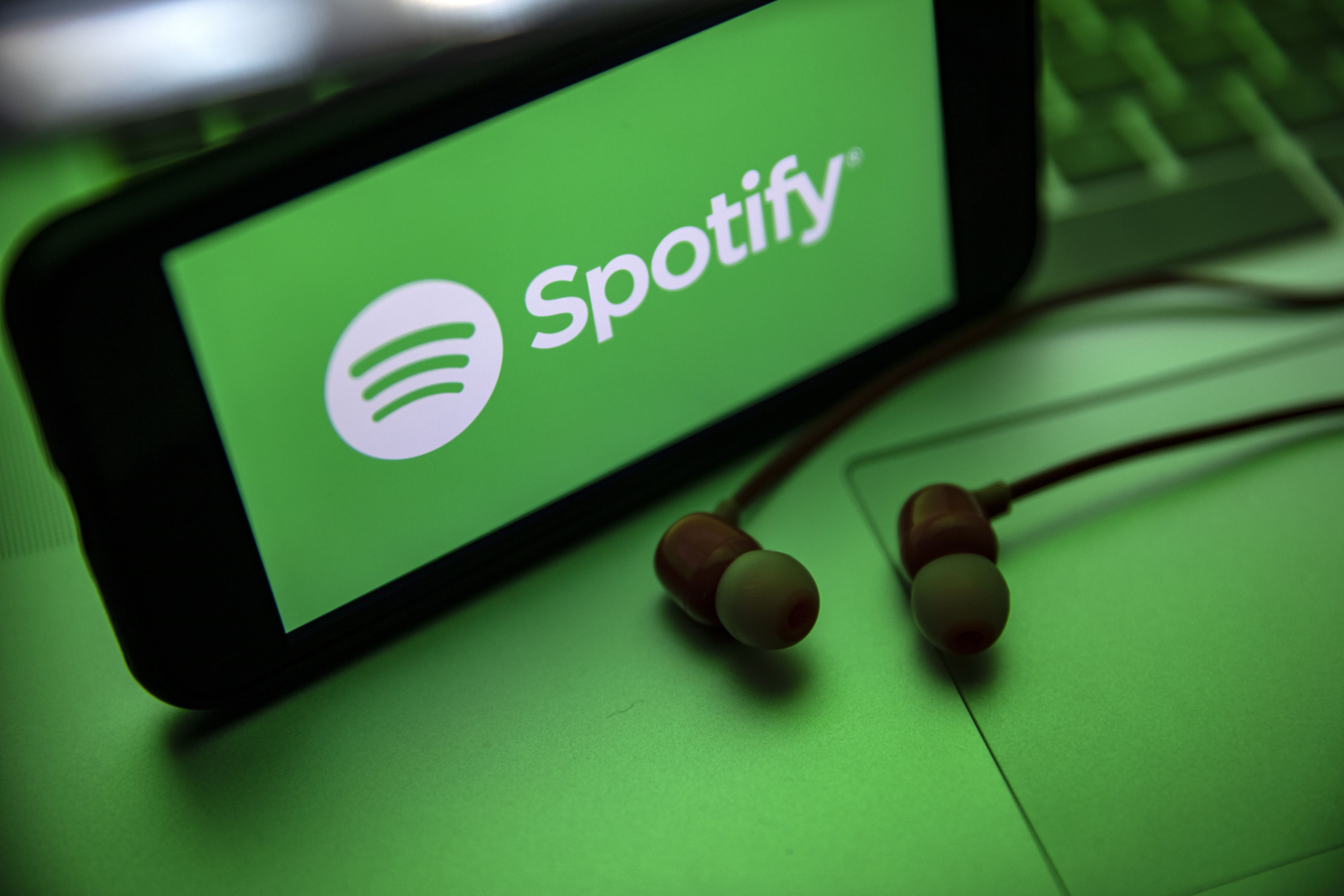 In this photo illustration the Spotify logo seen displayed on a smartphone screen near a pair of earphones.